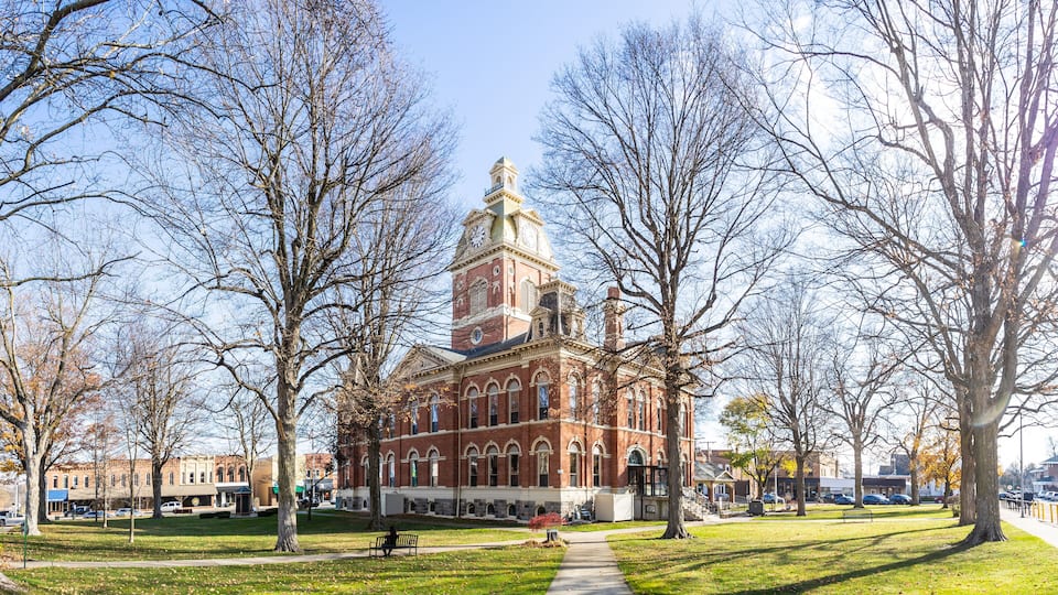 A historic brick building with a clock tower, surrounded by a park with trees and a pathway.