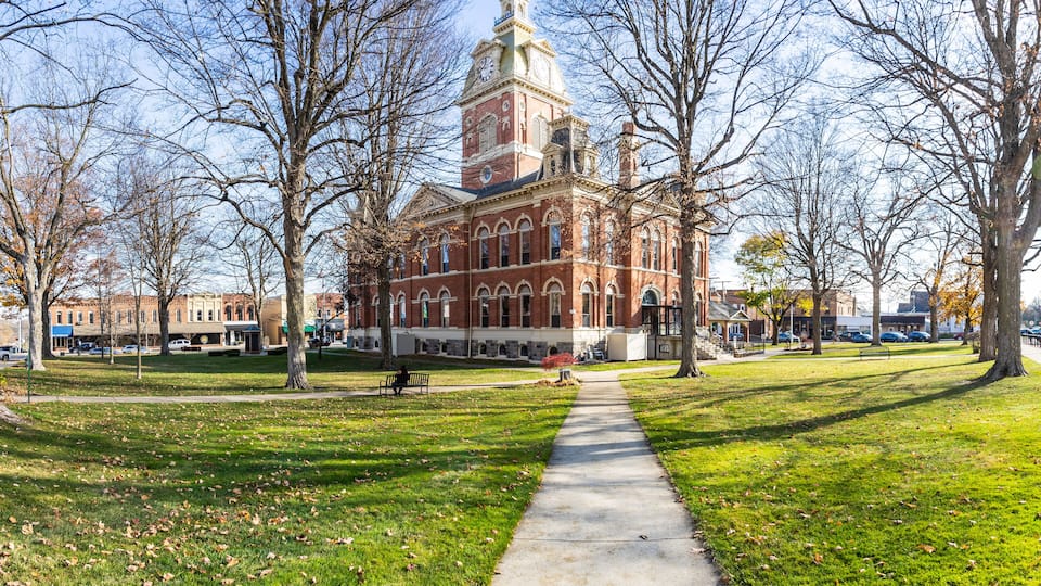 A historic building with a clock tower, surrounded by a park with a walking path and benches.