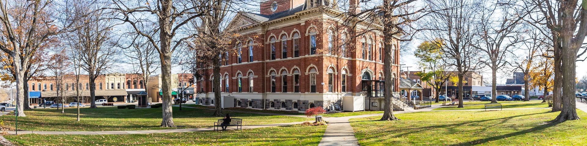 A historic building with a clock tower, surrounded by a park with a walking path and benches.
