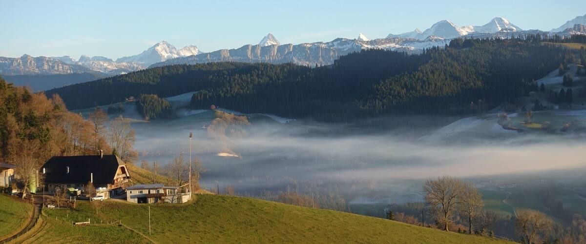 A mountainous landscape with a village, snow-capped peaks, and a valley shrouded in mist.