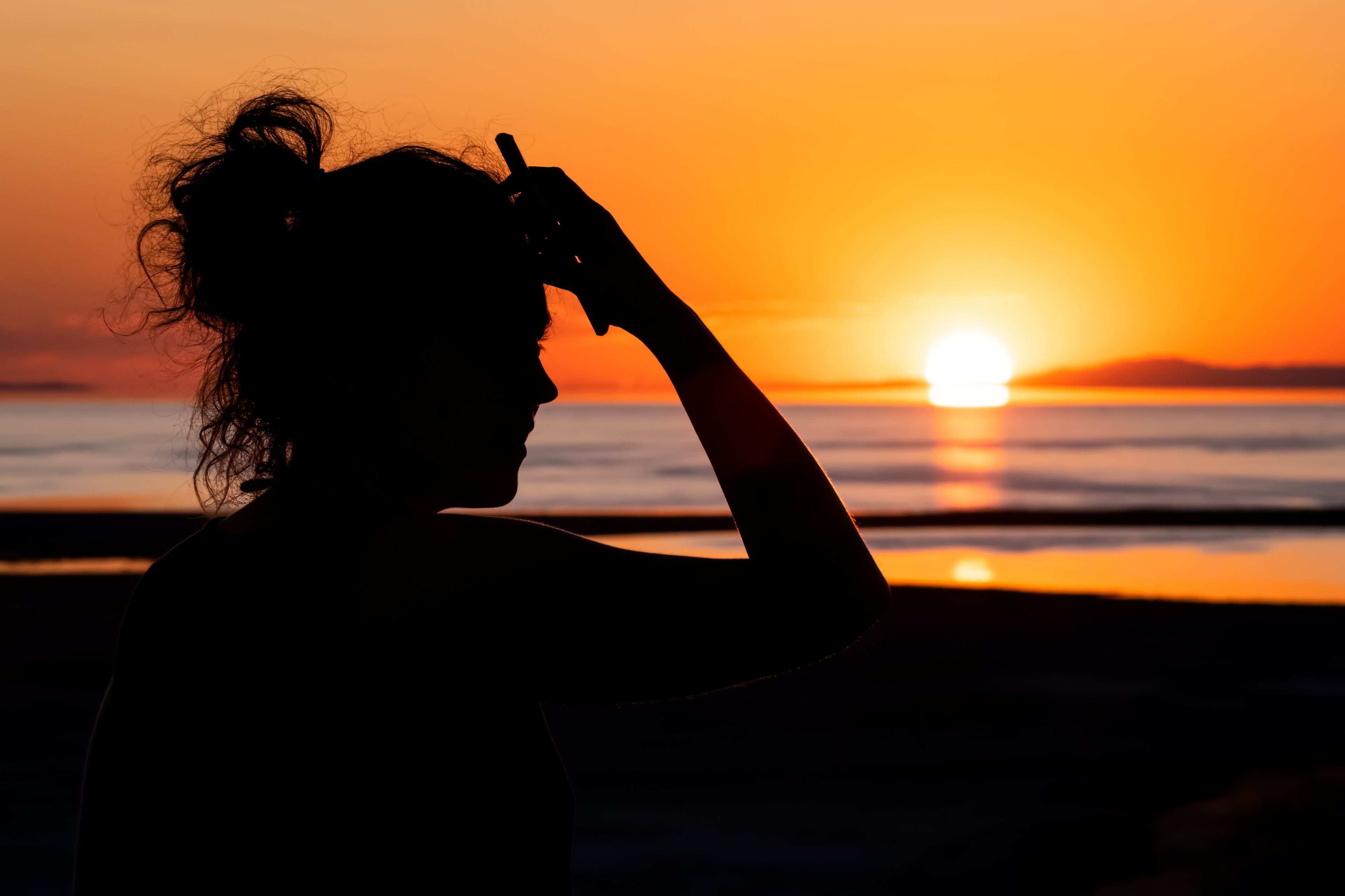 A silhouette of a person at sunset with the sun setting over the horizon.