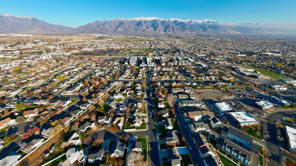 An aerial view of a town with residential areas, roads, and mountains in the background.