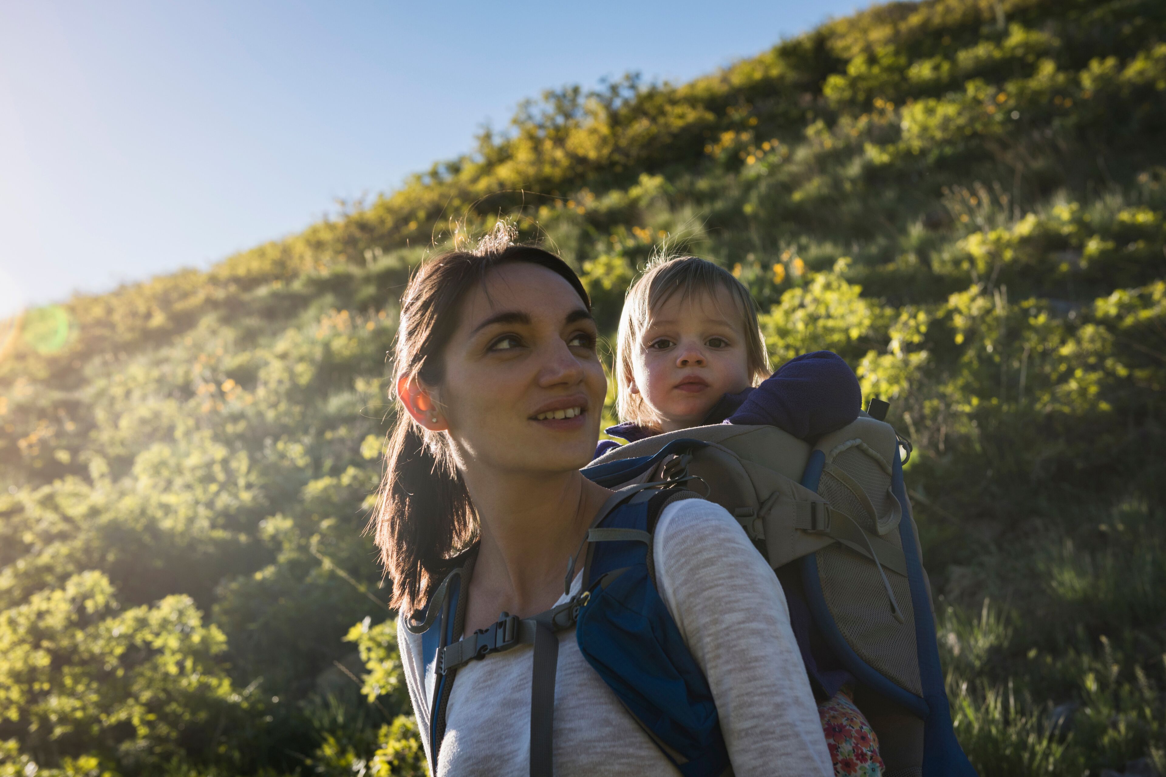 Mother carrying young daughter on back, hiking the Bonneville Shoreline Trail in the Wasatch Foothills above Salt Lake City, Utah, USA