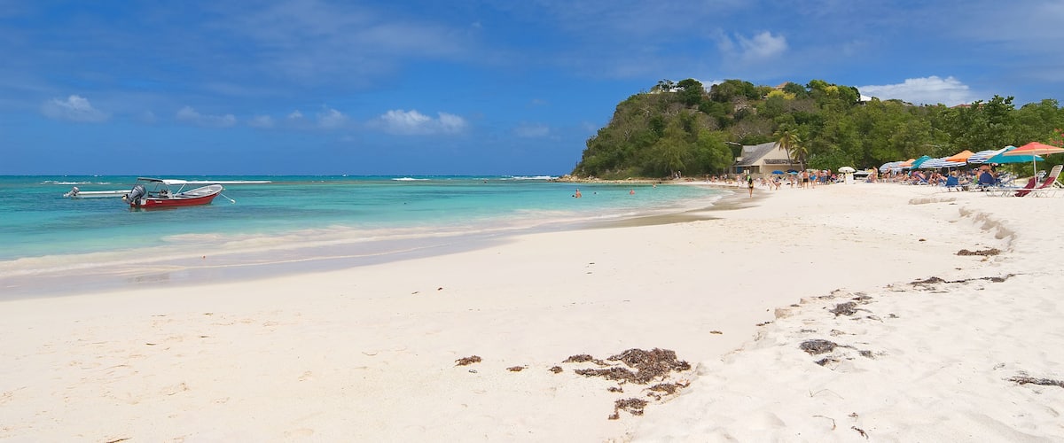 A beach with white sand, a red boat, and a clear blue sky.