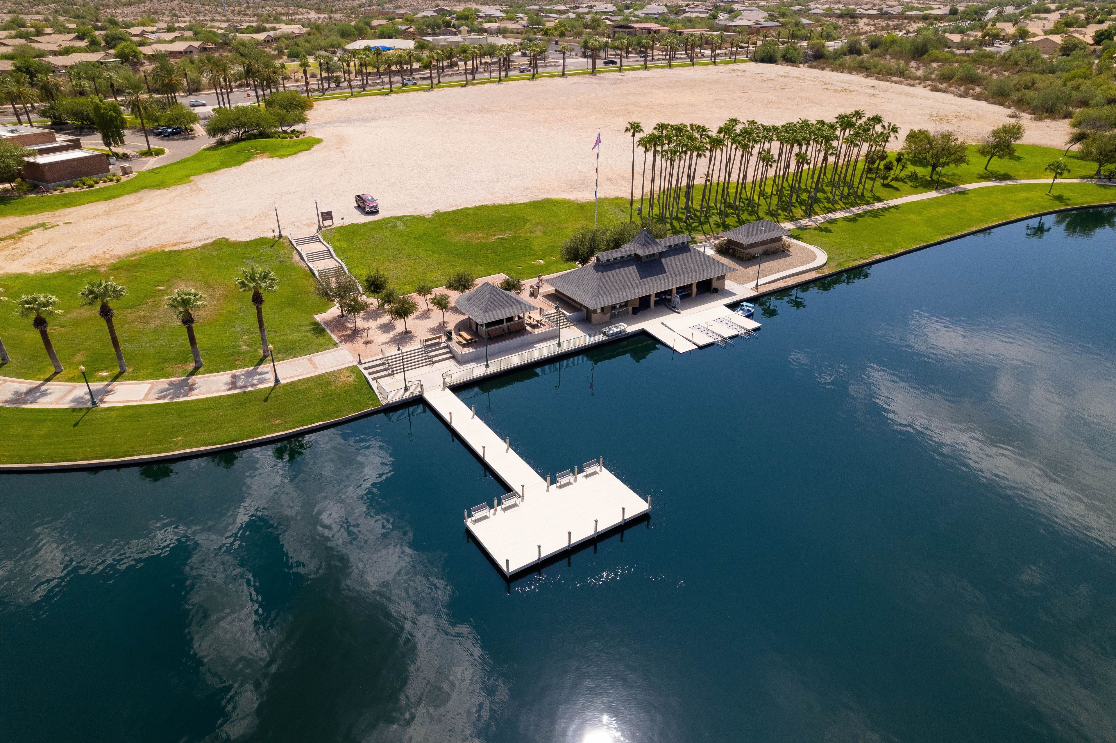 A marina with a dock extending into a calm body of water, surrounded by a landscaped area with palm trees and a sandy beach.