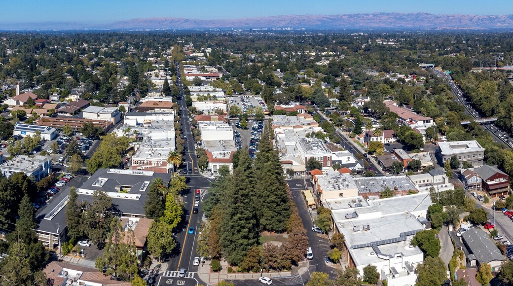 Aerial panoramic view of downtown Los Gatos with a mix of residential and commercial buildings. Highway 17 cuts through the suburban area with mountains in the background.
