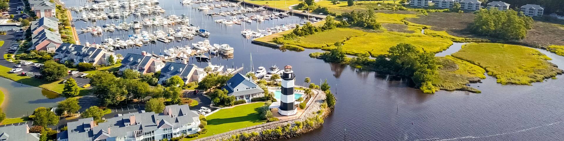 An aerial view of a marina with boats, a lighthouse, and surrounding residential buildings.