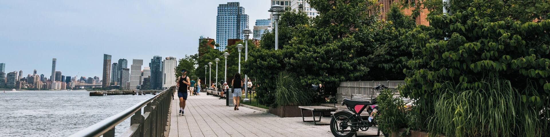 A riverside walkway with a city skyline, including a historic building and modern skyscrapers.