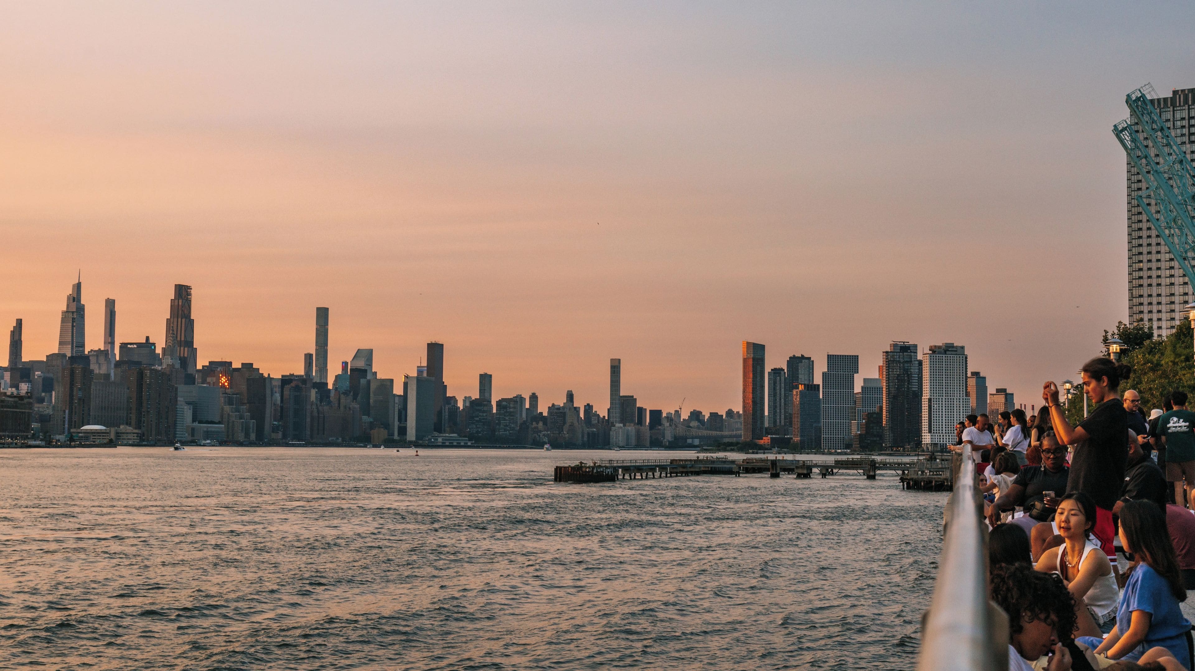 A city skyline at sunset with a waterfront promenade.