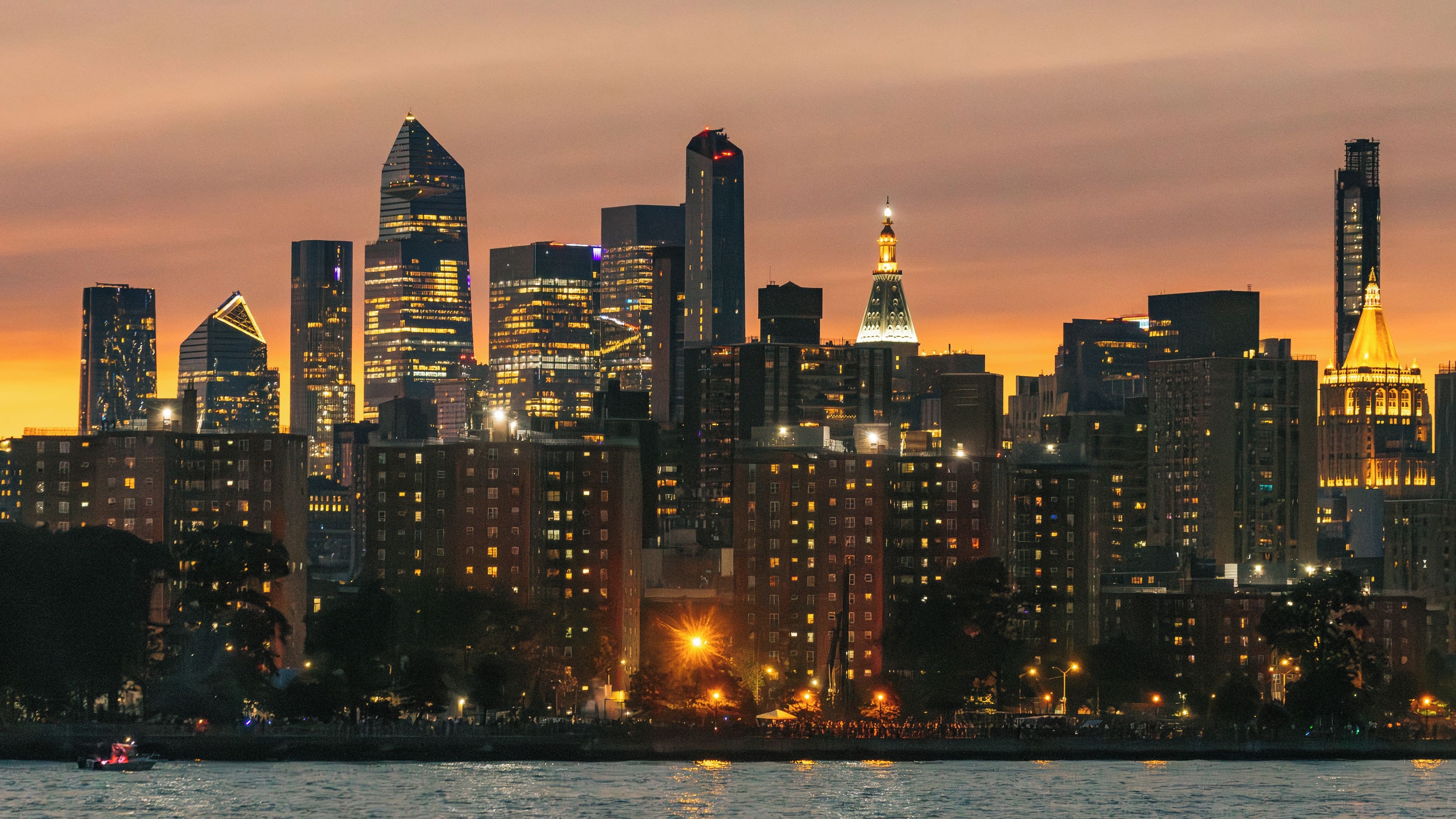 A city skyline with illuminated buildings against a sunset sky.