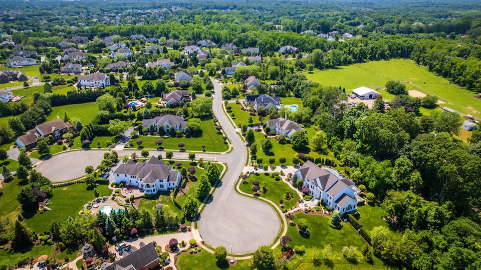 An aerial view of a suburban neighborhood with houses, green lawns, and a winding road.