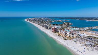 Vista aérea de uma cidade costeira com uma extensa praia, área urbana densa e águas azul-claras.