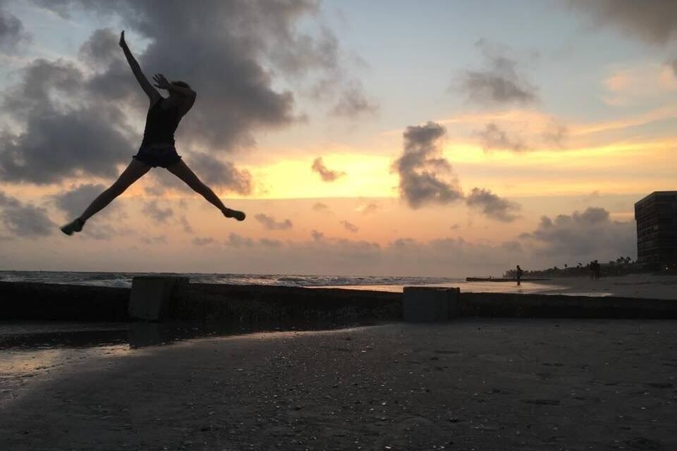 A person jumping on a beach with a sunset in the background.