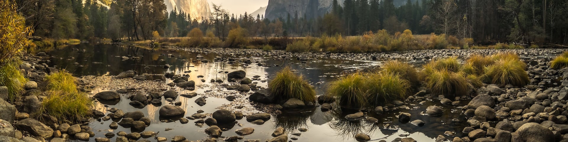 Un río con rocas y hierba, rodeado de montañas y árboles.