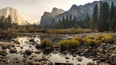 Un río con rocas y hierba, rodeado de montañas y árboles.