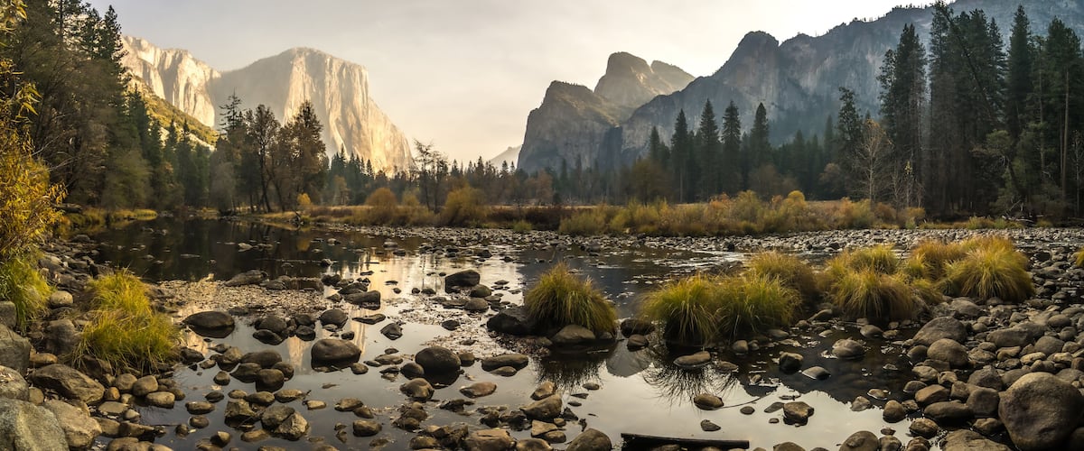 A river with rocks and grass, surrounded by mountains and trees.