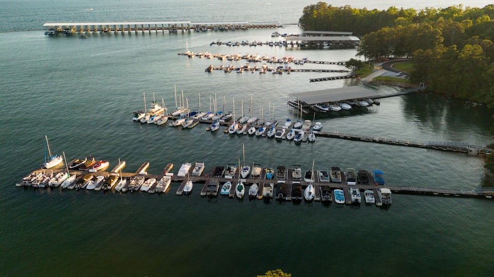 A marina with numerous boats docked at piers and a forested island in the background.