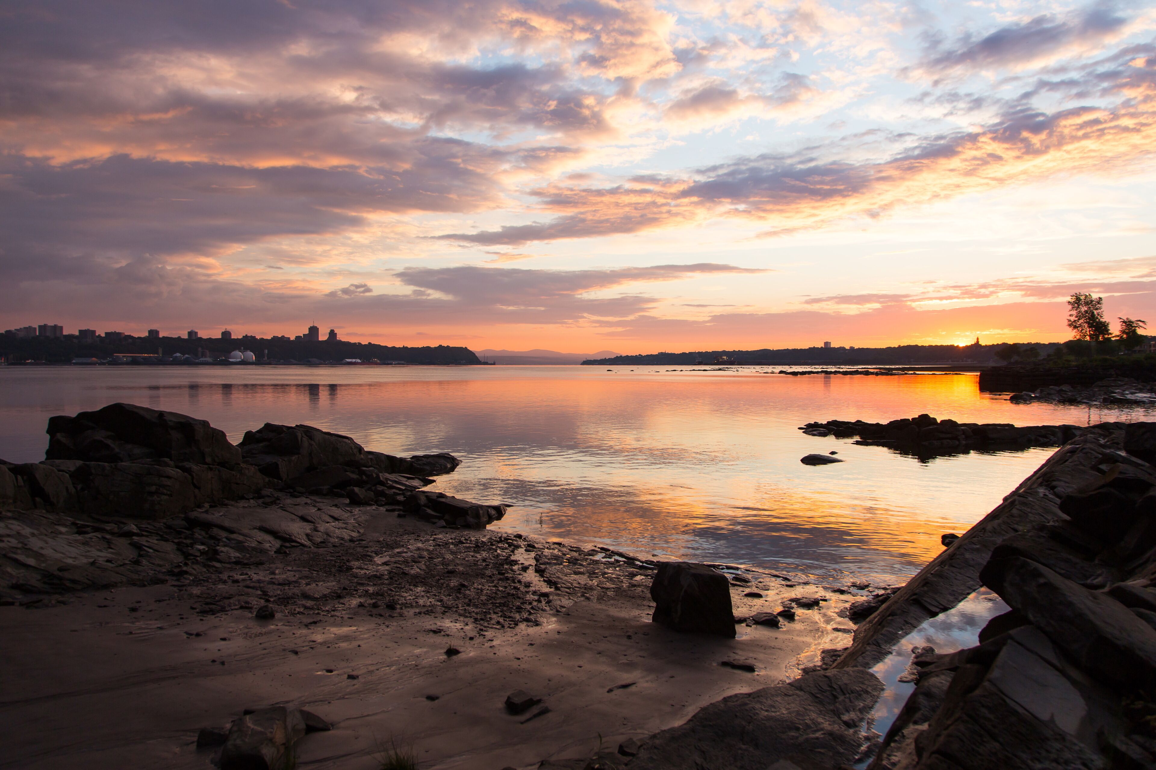 The St. Lawrence River north and south coastlines with Quebec City and Lévis skylines seen from a rocky beach during a summer sunrise, Quebec, Canada