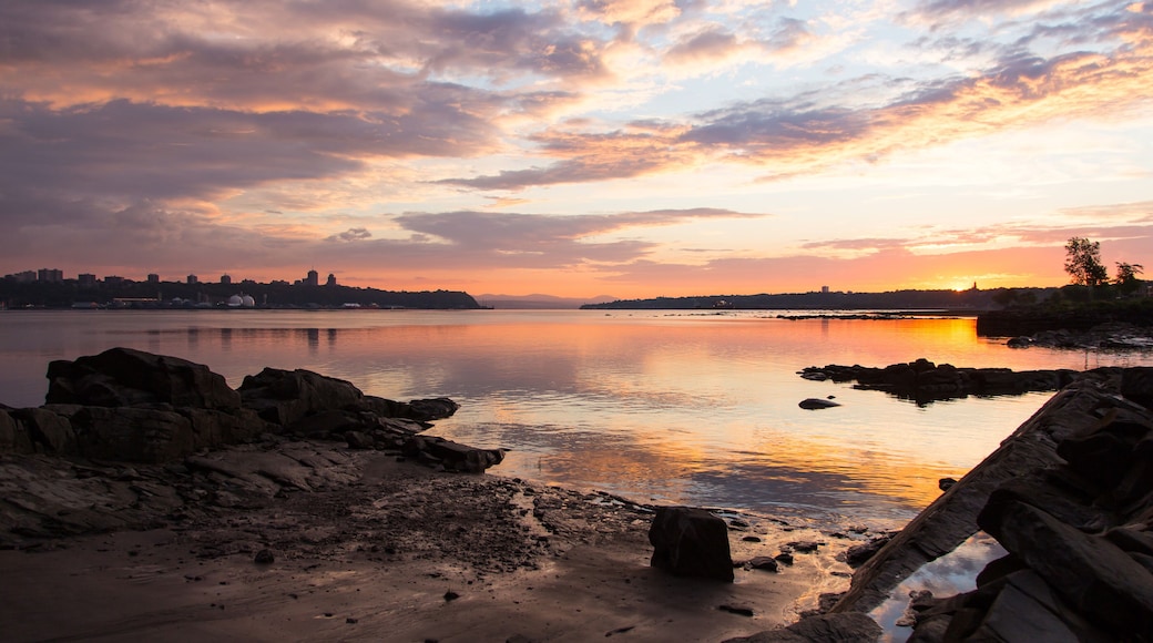 The St. Lawrence River north and south coastlines with Quebec City and Lévis skylines seen from a rocky beach during a summer sunrise, Quebec, Canada