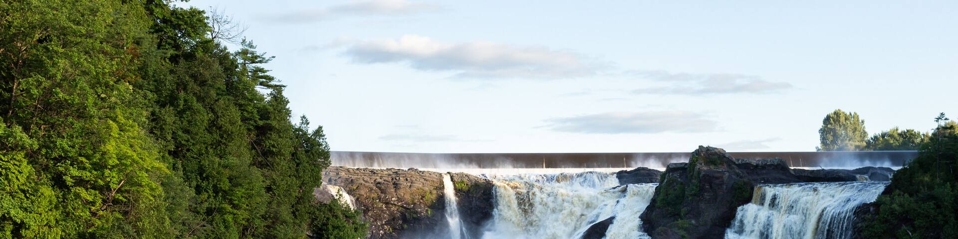 Back view of two young men hiking on the shore of the Chaudière River during a summer late afternoon, with the famous falls in the background, Lévis, Quebec, Canada
