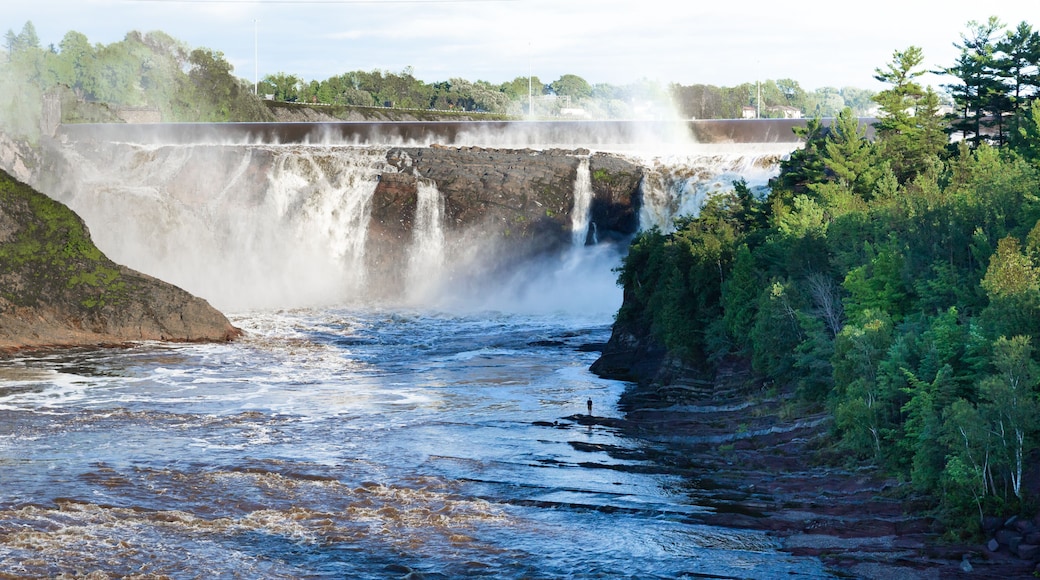 Tiny silhouette of young man standing on the shore of the Chaudière River during a summer late afternoon, with the famous falls in the background, Lévis, Quebec, Canada