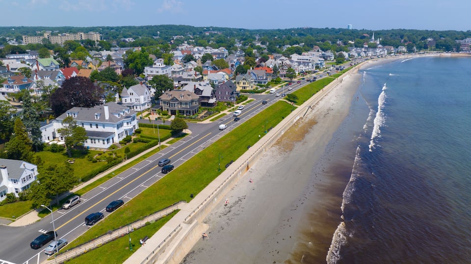 A coastal town with a wide beach, a road parallel to the shore, and residential houses.
