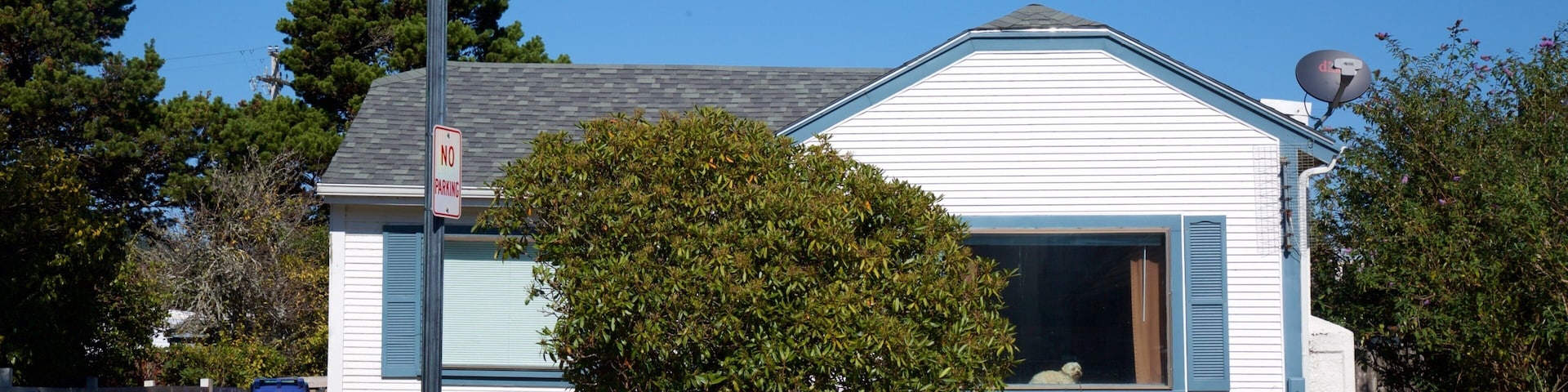 A white house with blue shutters, a white picket fence, and a 'No Parking' sign.