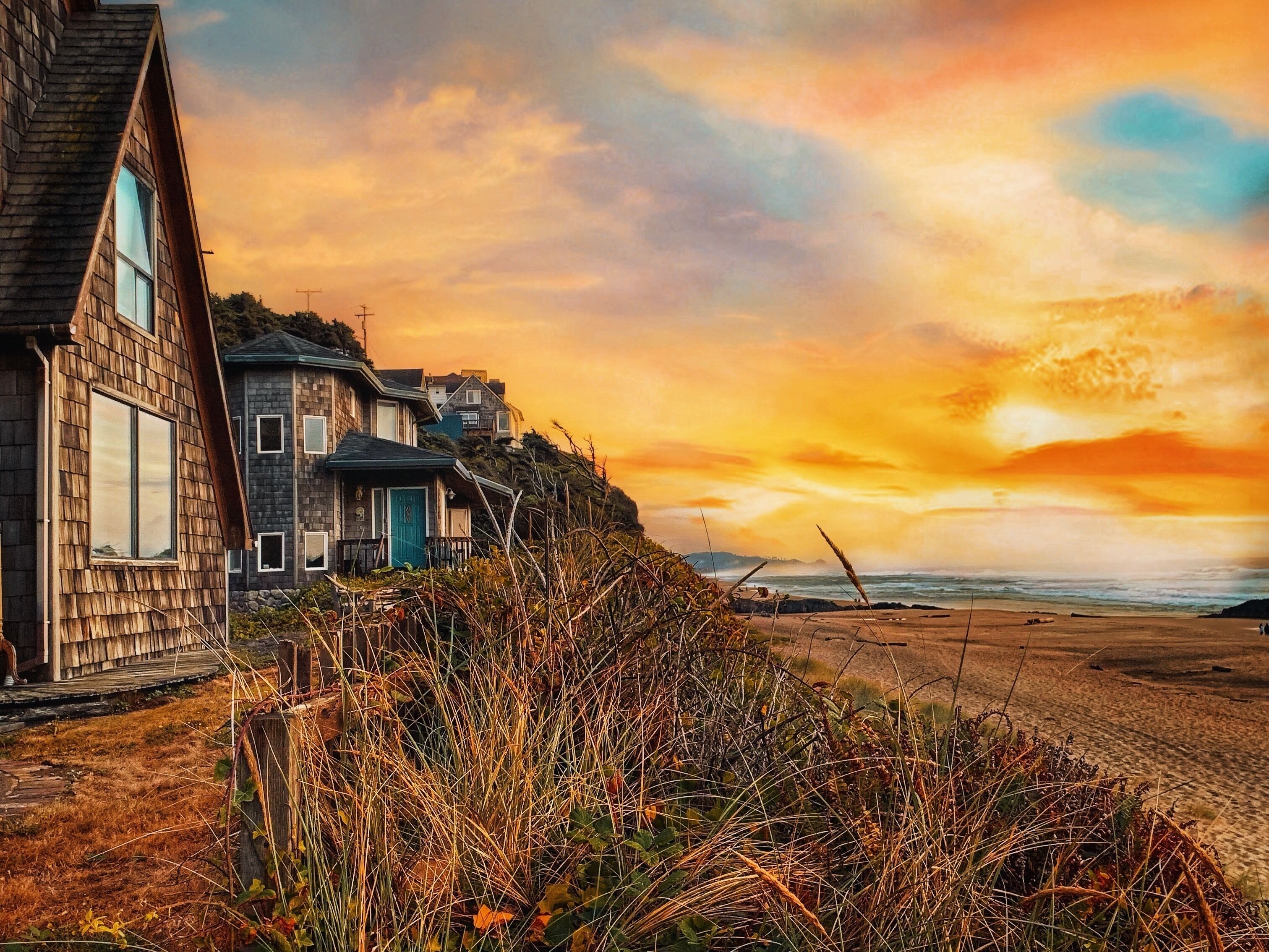 A coastal house with a steep roof, a wooden deck, and a view of the ocean during sunset.