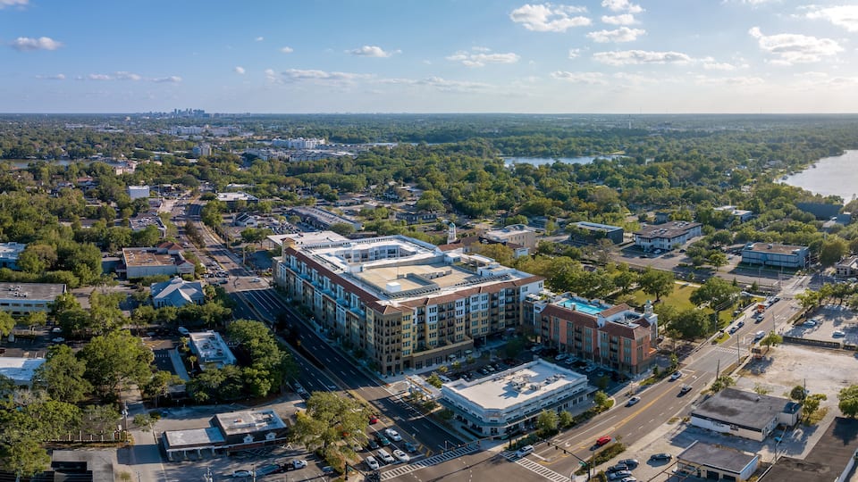 An aerial view of a city with a prominent building complex, surrounded by dense greenery and a river.
