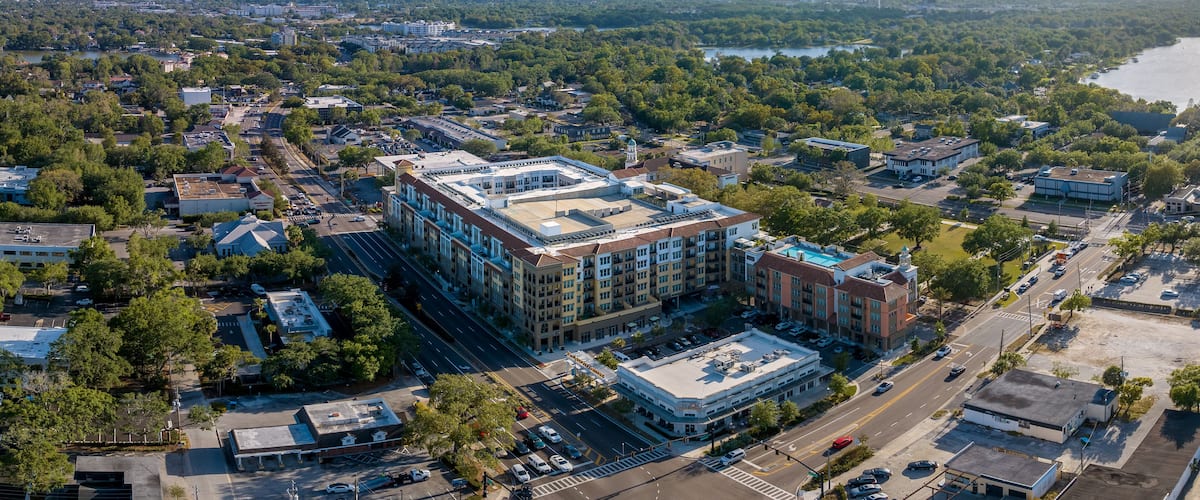 An aerial view of a city with a prominent building complex, surrounded by dense greenery and a river.