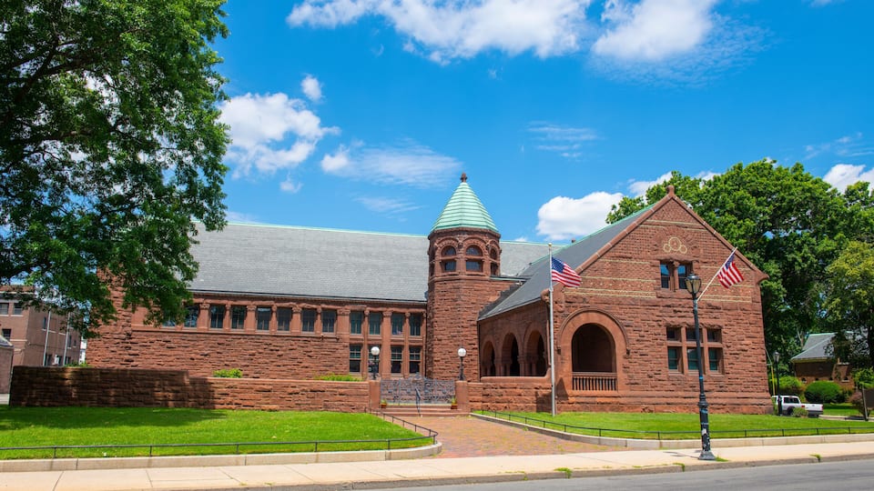A large brick building with a green roof and a tower, surrounded by green grass and trees.