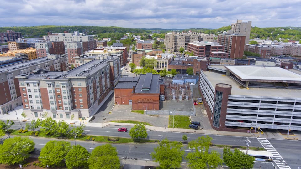 An urban landscape with multi-story buildings, a parking lot, and a road intersection.