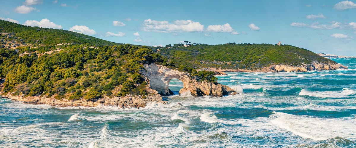 A coastal landscape with rocky cliffs, green hills, and a clear blue sea.