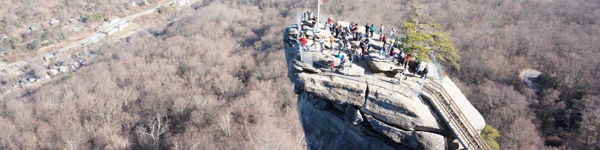 A rocky overlook with a flagpole, a river, and a trail.