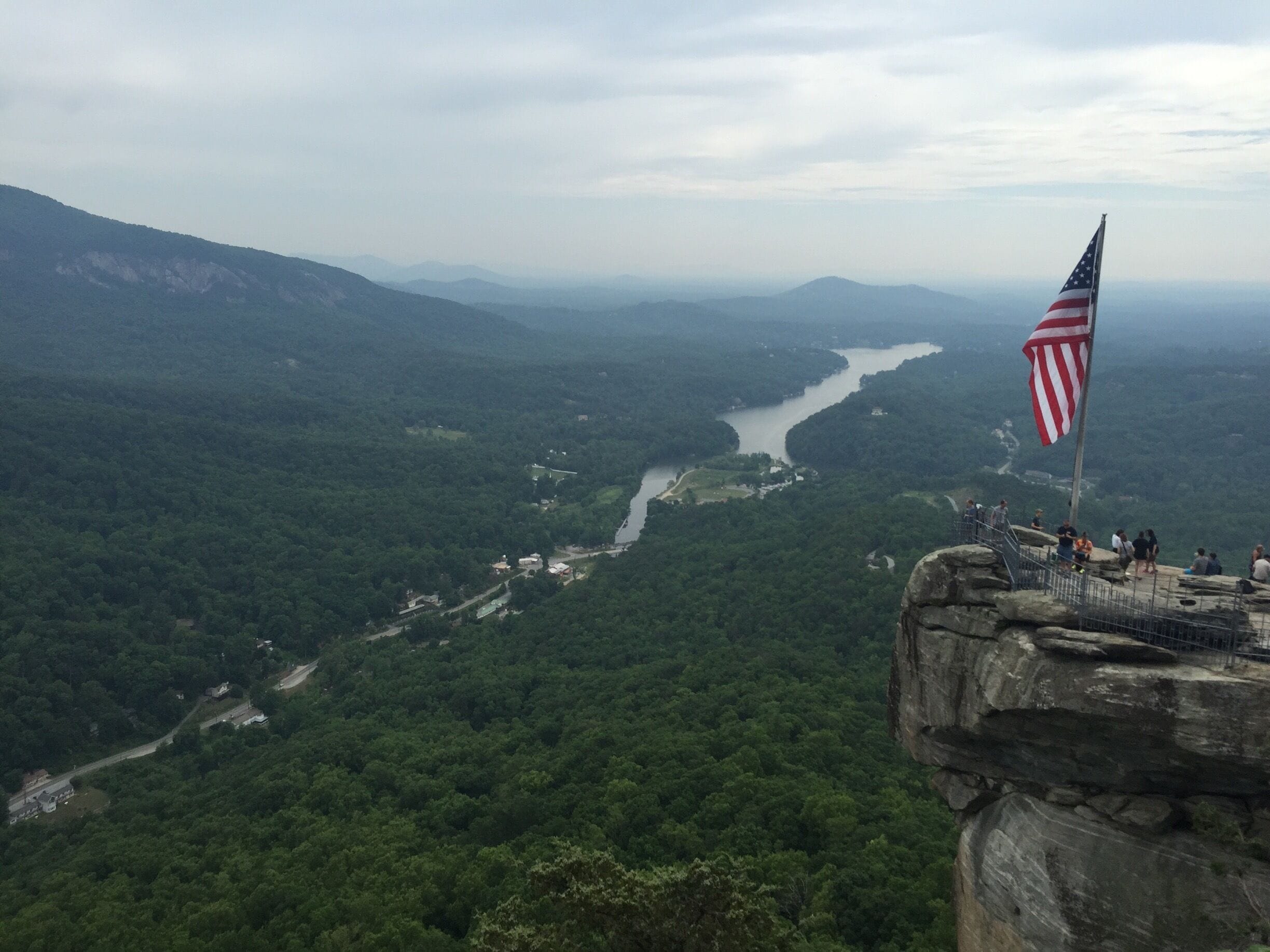 A river winding through a forested valley with a rocky overlook and an American flag.