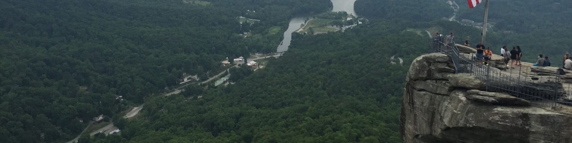 A river winding through a forested valley with a rocky overlook and an American flag.