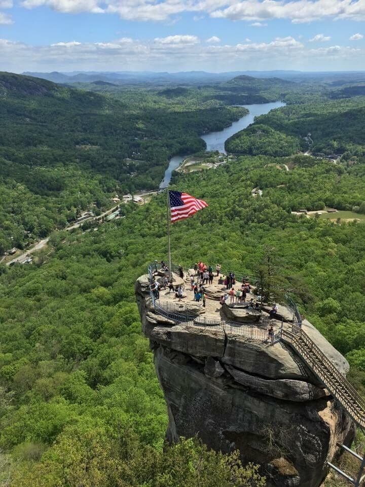 A viewpoint with an American flag on a rocky outcrop overlooking a river and forested valley.