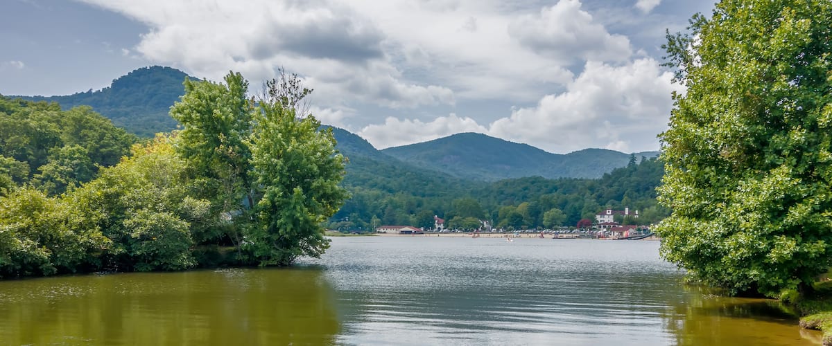 A lake surrounded by lush green trees and mountains in the background.