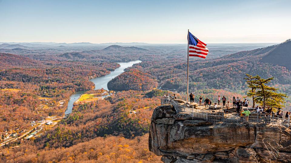 A river winding through a forested valley with a rocky outcrop and an American flag on top.