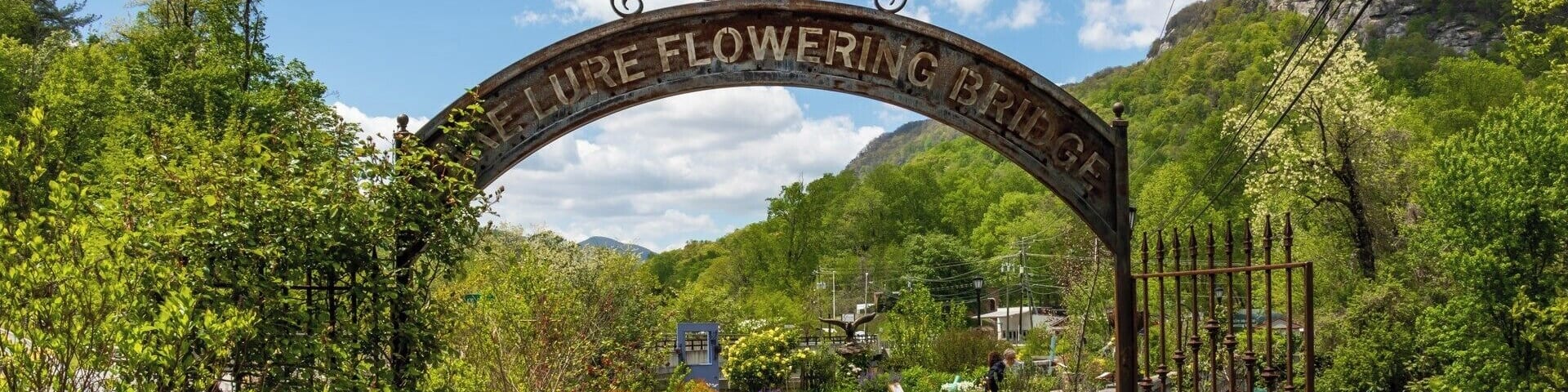 A pathway leading through a lush garden with a sign reading "Flowering Bridge."