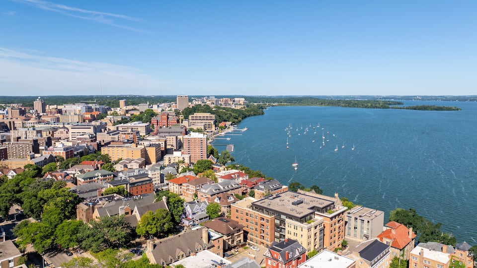 A coastal cityscape with dense urban buildings, a river, and sailboats.