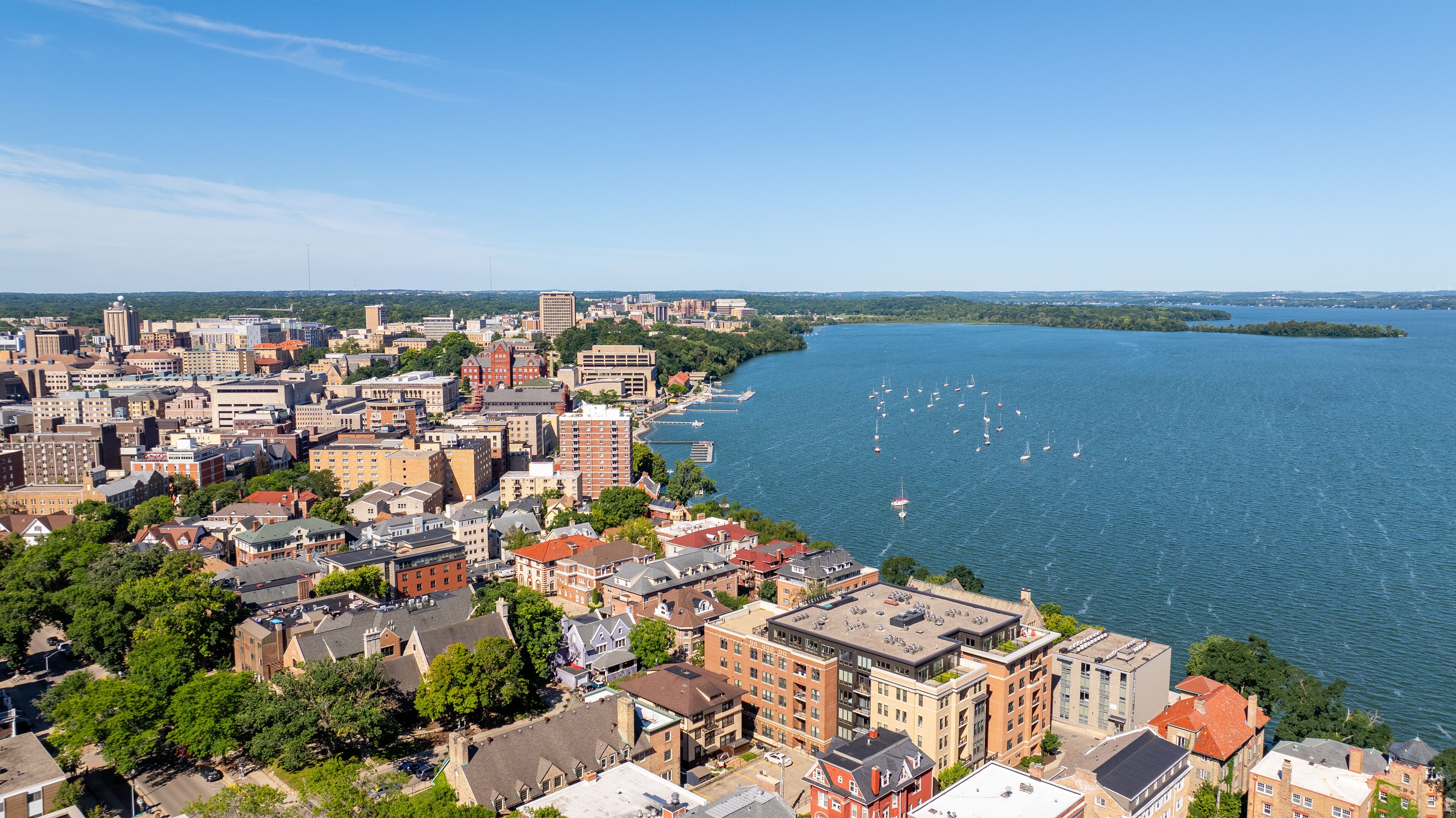 A coastal cityscape with dense urban buildings, a river, and sailboats.