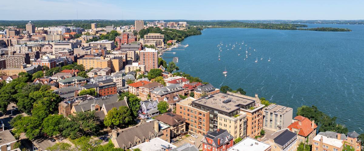A coastal cityscape with dense urban buildings, a river, and sailboats.