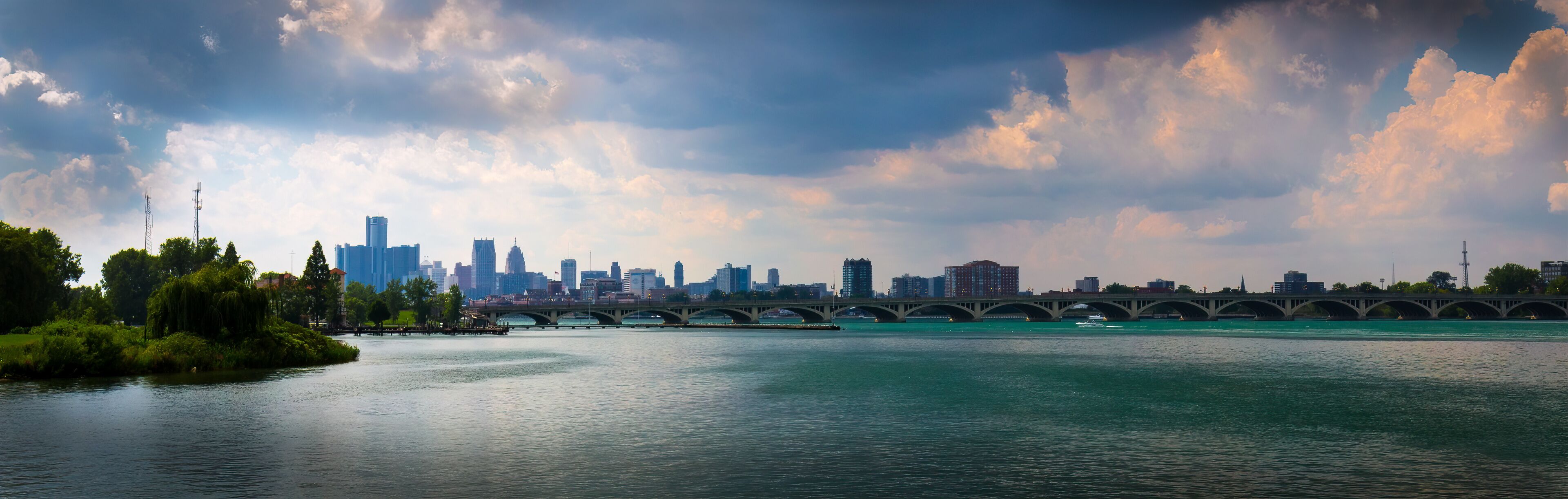 A river with a bridge, a city skyline, and a park with trees.
