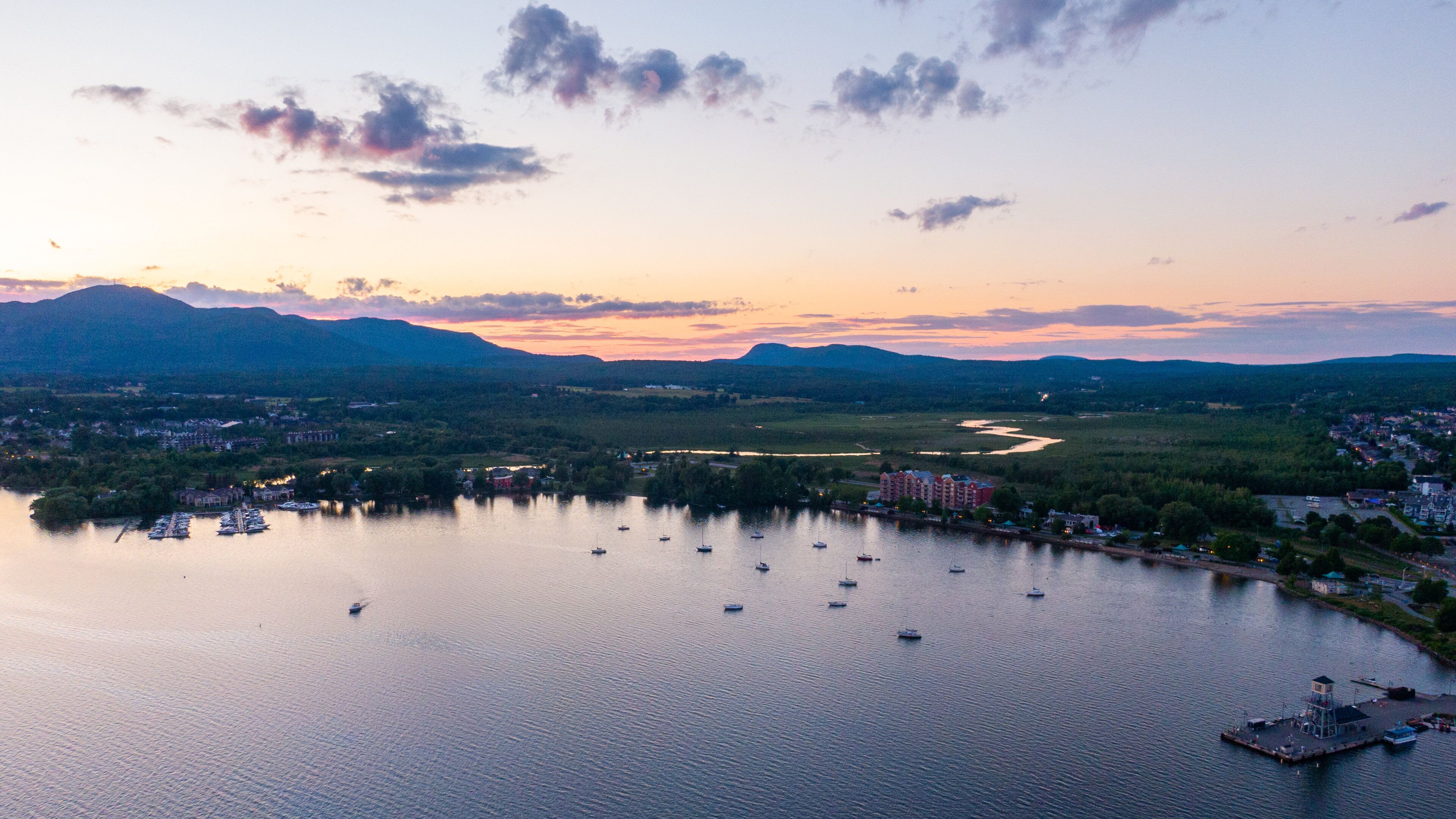A lake with boats, a dock, and a cityscape with buildings and mountains in the background.