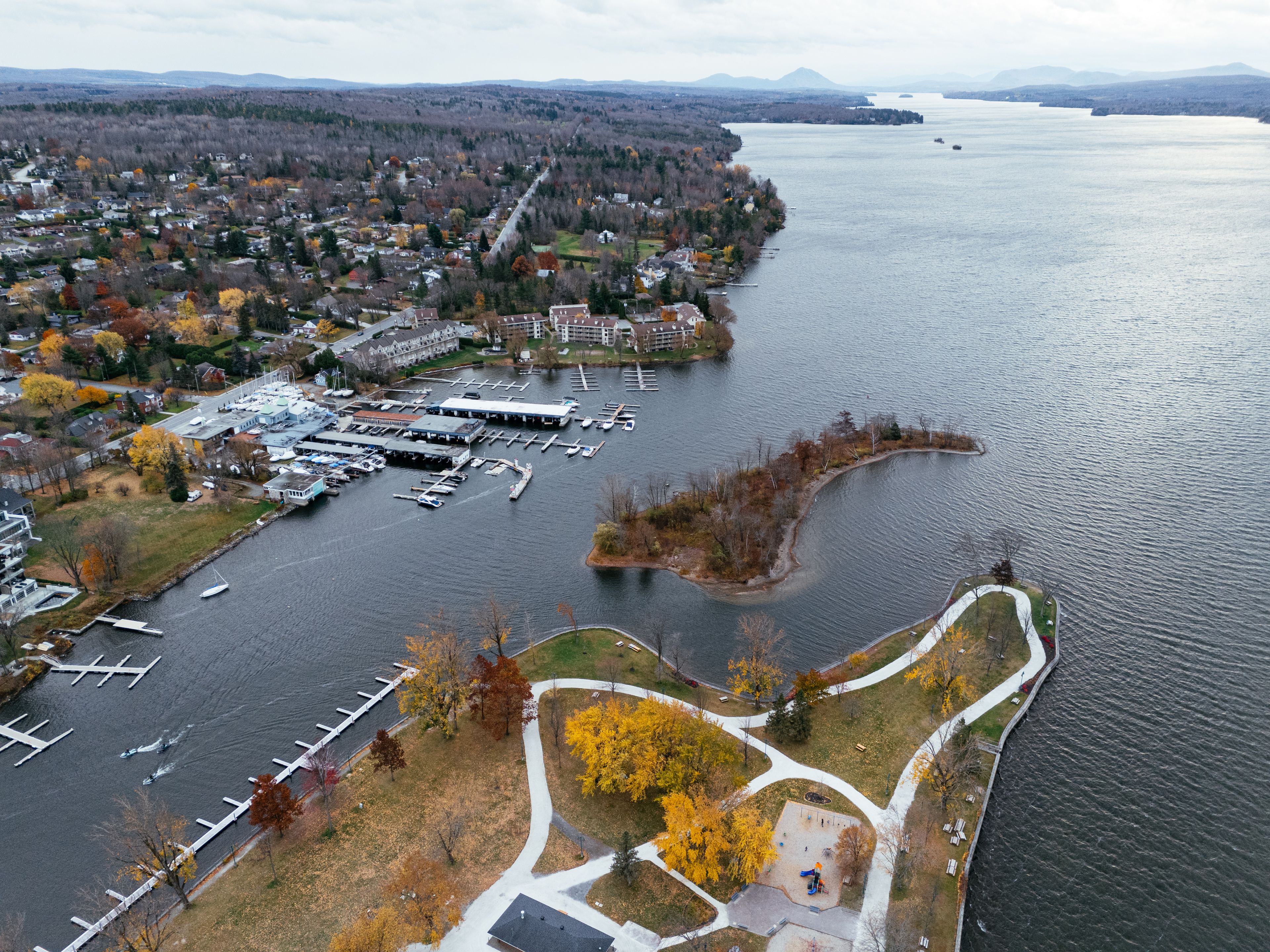 An aerial view of a lakeside town with a marina, waterfront park, and surrounding residential areas.