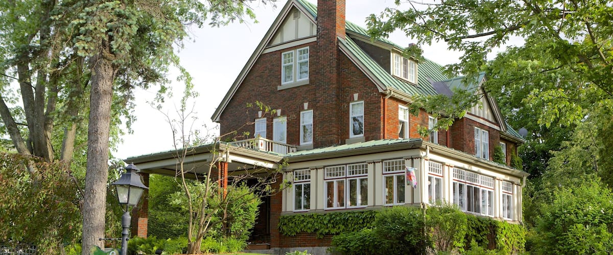 A large brick house with a green roof, surrounded by lush greenery and a paved driveway.