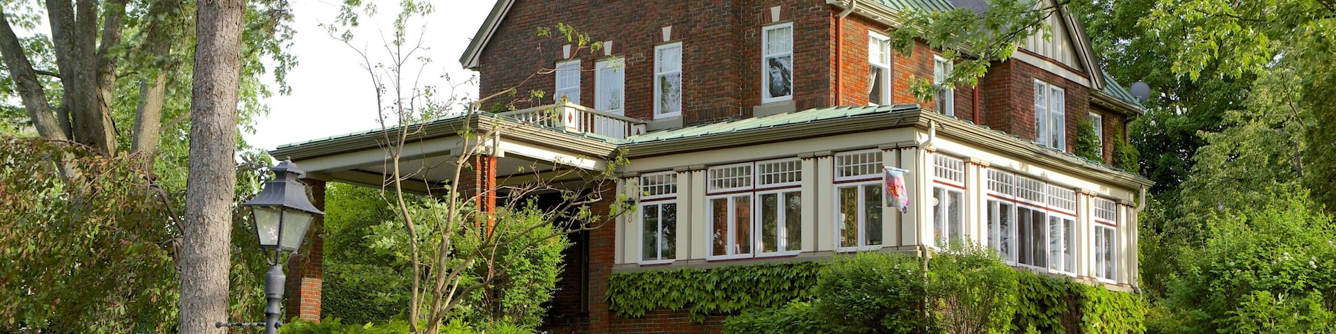 A large brick house with a green roof, surrounded by lush greenery and a paved driveway.
