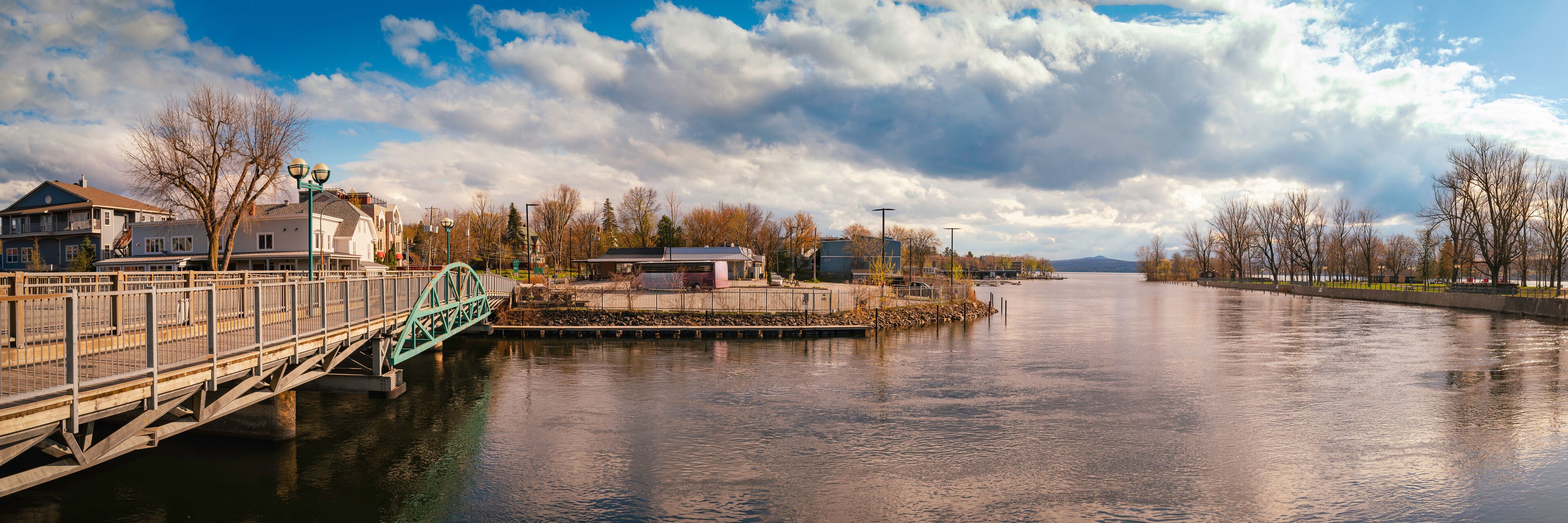 Magog city skyline, bridge, and houses at the marina next to Ponte-Merry Park in Quebec, Canada, with dramatic cloudscape over the bay