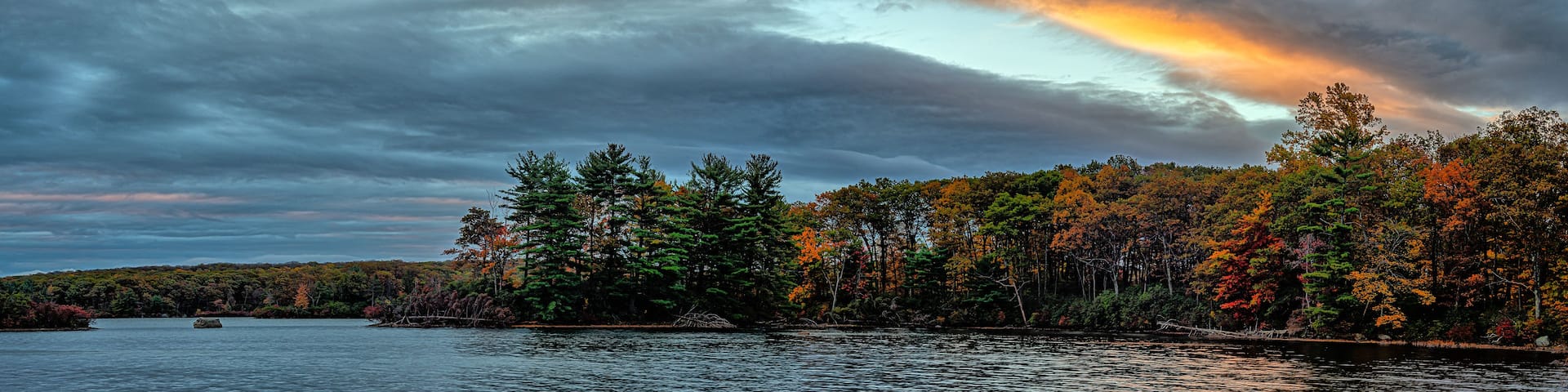 A lake surrounded by autumn-colored trees under a cloudy sky.